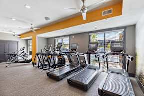 A gym with treadmills, elliptical machines, and a fan.
