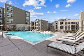 A large swimming pool surrounded by sun loungers and apartment buildings.