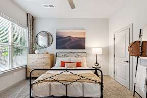 A bedroom with a bed, a dresser, a mirror, a lamp, and a painting on the wall.