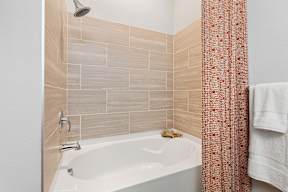 A white bathtub with a shower head and a towel hanging on the wall.