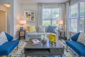 A living room with a blue couch, a grey sofa, a coffee table, and a painting on the wall.