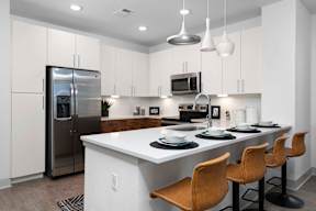 A modern kitchen with a white island and brown chairs.