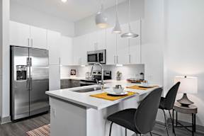 A modern kitchen with a white countertop and black chairs.