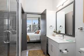 A bathroom with a sink, mirror, and a bedroom in the background.
