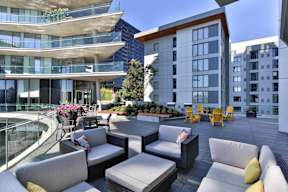A patio with couches and chairs is surrounded by modern buildings.