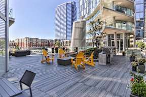 A wooden deck with chairs and a table in the foreground with a cityscape in the background.