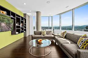A modern living room with a glass table and a grey couch.