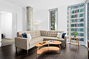 A living room with a grey couch, a wooden coffee table, and a large window.