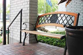 A wooden bench with a black metal frame sits on a brick patio.