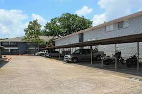 A parking lot with a grey building in the background and a car parked in front of it.