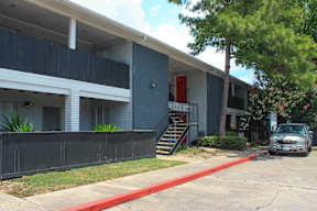 A grey building with a red door and a car parked in front.
