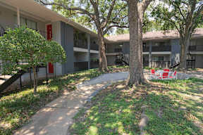 A tree in front of a building with a red door.