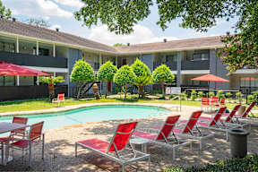 A pool area with red chairs and trees.