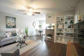 A living room with a couch, a coffee table, a rug, a ceiling fan, and a bookcase.
