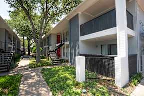 A white apartment building with a red door and black railings.