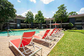 A row of red lawn chairs are lined up on a concrete patio next to a pool.
