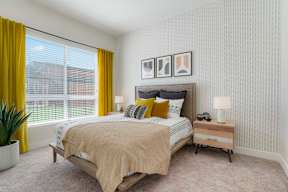 A bedroom with a bed, nightstand, and a window with yellow curtains.