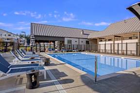 A swimming pool area with sun loungers and a building in the background.