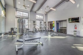 Large fitness center with concrete flooring and ceiling fans. Weight benches, yoga balls, and cardio machines