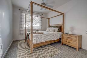 A bedroom with a four-poster bed, striped bedspread, and a small nightstand with a lamp.