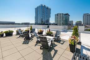 A rooftop patio with chairs and tables overlooking a cityscape.