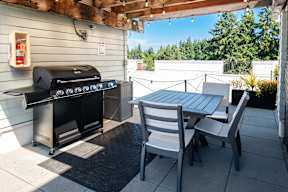 A black grill is on a patio with a table and chairs.
