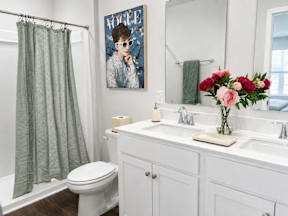 A bathroom with a white toilet, a sink with a vase of flowers, and a poster on the wall.