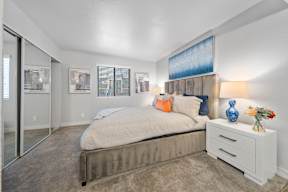 A bedroom with a bed, nightstand, and artwork on the wall.