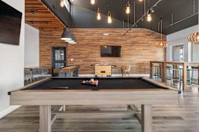 A pool table is in the middle of a room with a wooden wall.