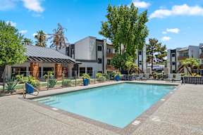 A swimming pool in front of a building with a fence and trees.