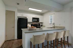 A kitchen with a black fridge, microwave, and a bowl of fruit on the counter.