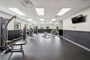 A gym with a variety of equipment including a treadmill, weights, and a television.