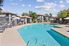 A swimming pool surrounded by sun loungers and umbrellas.