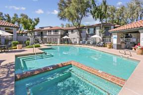 A swimming pool surrounded by a patio with chairs and umbrellas.