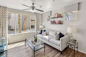 A living room with a grey couch, a glass coffee table, and a ceiling fan.