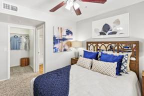 A bedroom with a bed, pillows, a ceiling fan, and a painting on the wall.