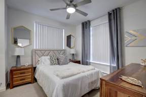 A bedroom with a large bed, a ceiling fan, and a wooden dresser.