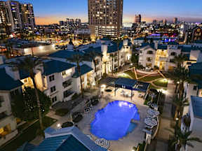 A swimming pool surrounded by palm trees and buildings at dusk.