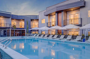 A large swimming pool in front of a modern building with sun loungers.