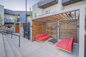 A modern outdoor seating area with red cushioned benches and a wooden slatted gate.