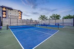 A tennis court is surrounded by a fence and a building.