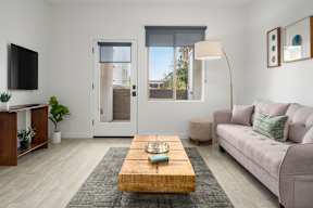 A living room with a grey couch, a wooden coffee table, and a flat screen TV mounted on the wall.