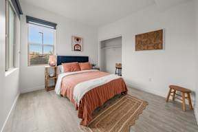 A bedroom with a bed, a window, and a wooden stool.
