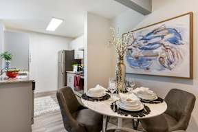 A dining room with a table set for two and a painting on the wall.