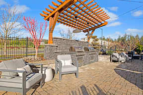 A patio with a wooden pergola and grey couches.