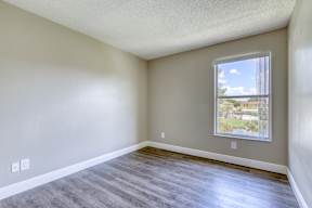 A room with a window showing a view of a fence and a building outside.