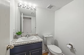 A bathroom with a sink, mirror, toilet and lights on the mirror.