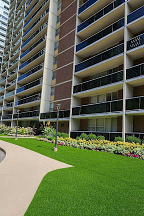 A tall building with balconies and a green lawn in front.