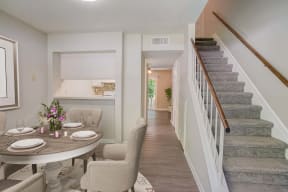 a dining area with a table and chairs and a staircase in the background