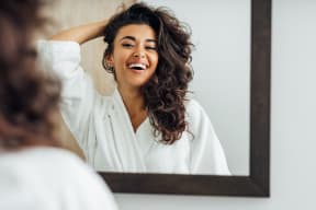 a woman laughing in front of a mirror with her hand on her hair